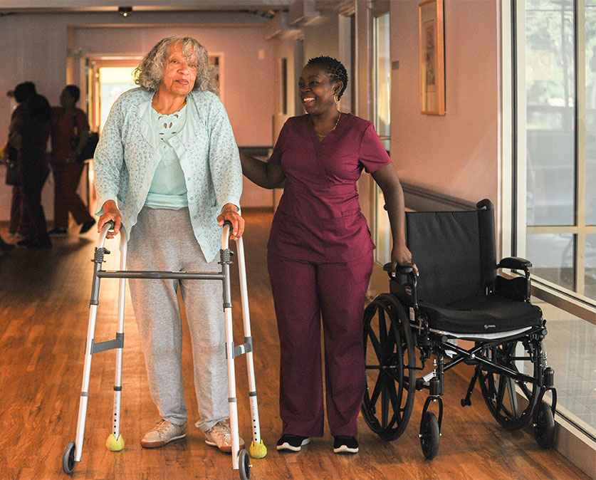 A woman in scrubs standing next to a lady with a walker.